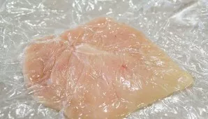 First turn on the oven, let it heat up to 220 degrees. Rinse the chicken, dry it and carefully beat it under the cling film.