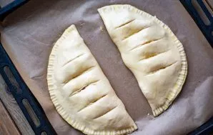 Lay out two calzones on a baking sheet, make several incisions on each so that steam comes out, brush the surface with a beaten egg and p...