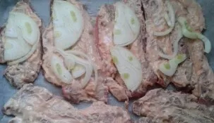 Cover the baking sheet with baking paper and add the pork. Cut the onion into half rings and put it on top of the meat.