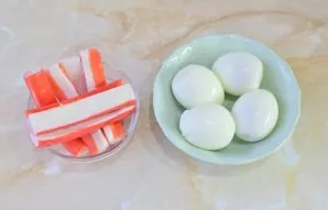 Pre-boil the eggs in boiling water for 7-8 minutes. Then cool them in cold water. Peel the cooled eggs. Remove the crab sticks from the p...