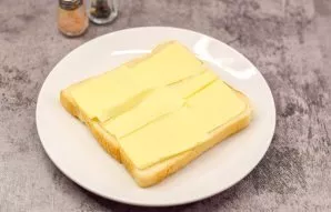 Grease the first slice of bread with butter.