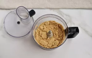 Without interrupting the process, add a little melted and cooled butter. Stir until the mixture looks like wet sand.