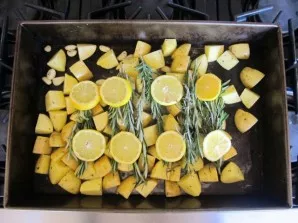 Lay out potatoes with garlic on a baking sheet, put slices of rosemary and lemon on top.