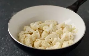 Rinse the cauliflower, sort it into inflorescences. Add to the fried onions and garlic, fry until tender, covering for about 8-10 minutes.