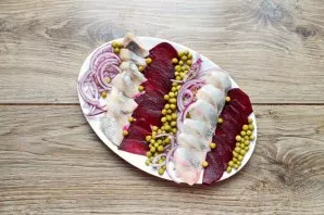 Next, layer the onion, herring, beets and peas. Pour vegetable oil on top of the snack.