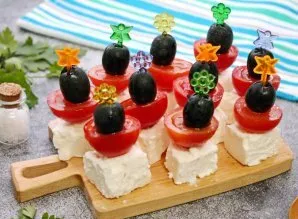 Using a skewer, pierce the olive, then half the tomato and the cheese. Garnish with herbs and serve.