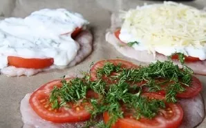 Put the cutlets on a baking sheet, salt, pepper, put tomatoes on top, sprinkle with herbs. Coat evenly with yogurt and sprinkle with cheese.