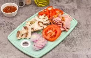 While the base is baking, chop the bacon, cut the tomatoes and onions into rings, and cut the mushrooms and bell peppers into slices.