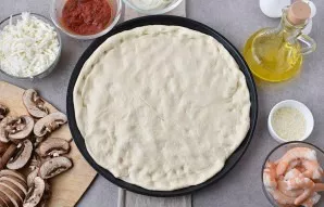 Turn on the oven to heat up to 250-260 degrees. Knead the risen dough and place it in the pizza pan with your hands.