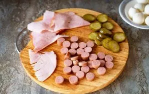 During this time, cut the sausages into thin slices, and also cut the pickled cucumber into thin slices and the ham into thin slices.