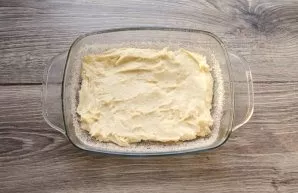 Grease the baking dish with vegetable oil, sprinkle with breadcrumbs and transfer half of the dough, level it.