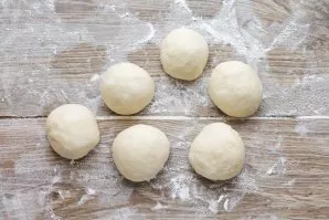 Divide the risen dough into equal pieces and form balls. Cover the dough with a towel and let rest for 10 minutes.