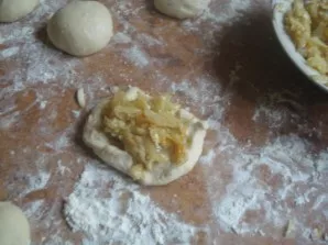 Put flour on the work surface and form small balls from the dough. Roll out each ball and place the stewed cabbage filling in the middle.