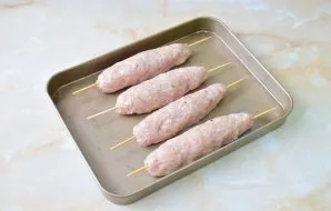 Grease your hands with vegetable oil and form meat sausages on wooden skewers. Grease the baking sheet with vegetable oil and put skewers...