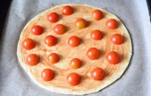 Coat the dough with a thin layer of tomato sauce and put cherry tomatoes on top, cut into two halves.