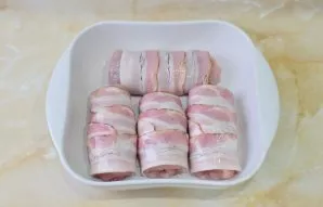 So roll up all the rolls and wrap them with strips of bacon. Grease the baking dish with vegetable oil and put rolls in it. Grease the to...