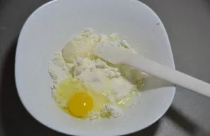 Break an egg into the cottage cheese, add a pinch of salt and granulated sugar.