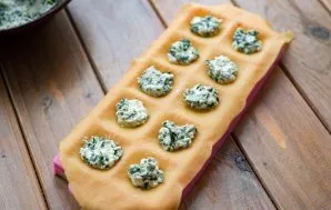 Put a thin layer of dough on the mold and put about a teaspoon of cottage cheese and spinach filling in each pit of the mold.