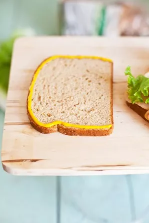 Apply mustard to the edges of the bread and put it on top of the sandwich.